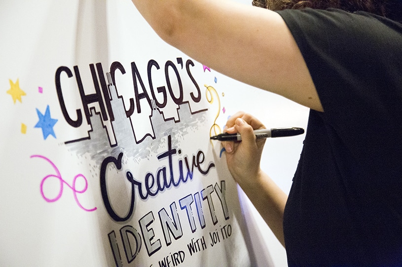 An artist draws a title of a graphic recording on a board