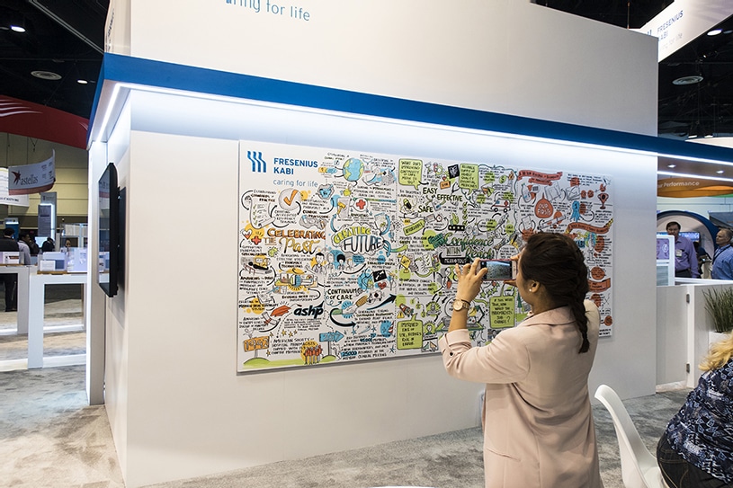 An attendee snaps a photo of Ink Factory's visual notes at the Fresenius Kabi conference booth